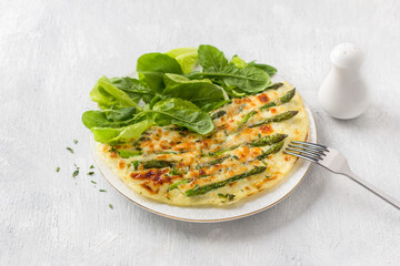 Delicious omelette with asparagus and cheese on a white plate on a light gray background, top view. Homemade vegetarian food