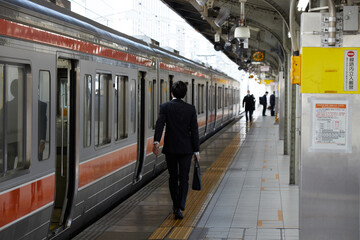 名古屋駅の朝の通勤電車とホームで歩く若いサラリーマンのうしろ姿