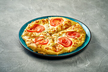 Khachapuri with salty melted cheese and tomato in a plate. Concrete background
