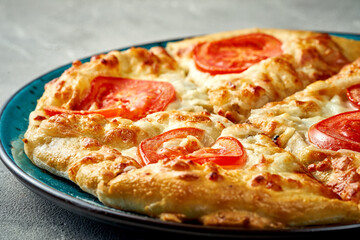 Khachapuri with salty melted cheese and tomato in a plate. Concrete background