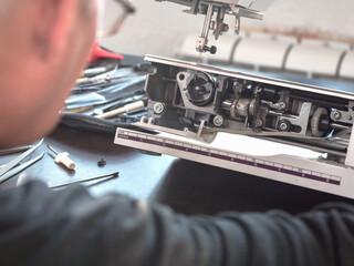 Male master repairs the sewing machine. Inspection of the mechanism in search of a breakdown....