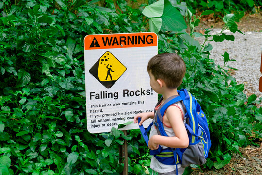 Young boy standing by warning sign on hiking trail