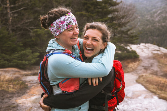 Two smiling female hikers embracing, Mt Willard, New Hampshire, USA