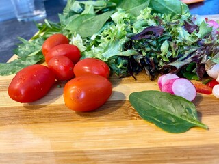 Salad greens tomatoes basil onions raddish on cutting board