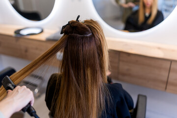 From above back view of unrecognizable female client sitting near mirror in beauty salon during...