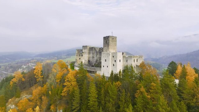 Slovak castles: an aerial view of Strečno Castle, towering on a cliff above the valley with the river Váh. Autumn, colourful leaves, mists in the valley, stone guard castle above the hilly landscape. 