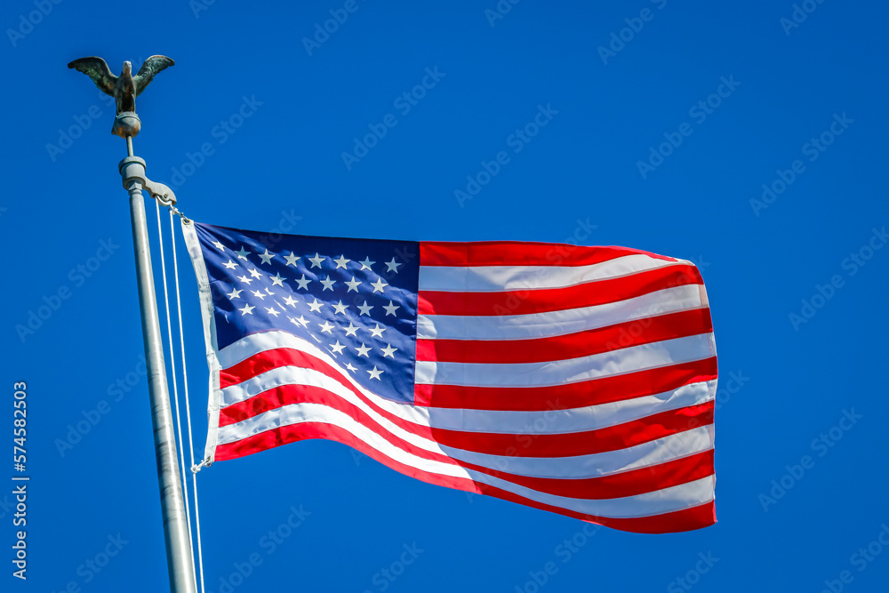 Wall mural american flag waving on pole with eagle and bright colors against blue sky