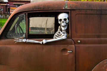 Human skeleton sitting in a rusty old car and looking out of the window