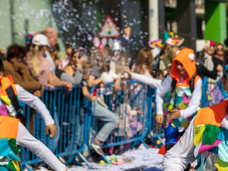 Blurred view of carnival parade on the street with unrecognizable people and artificial snow foam spray