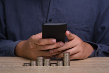 successful businessman in shirt holding mobile smartphone with stack of coins. managing investments, medical insurance payments in mobile banking application icon, personal savings expenditures.