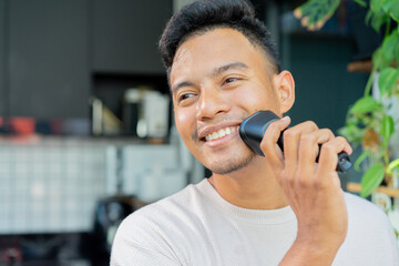 close up adult man use electric shaver to trimming beard on face at home in the morning for...