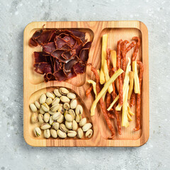 Snacks for beer. Pistachios, cheese, sausages and dried meat. On a wooden plate. Rustic style.