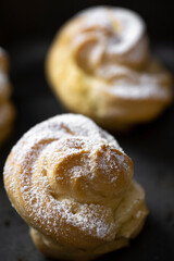 Decorating profiteroles with powdered sugar. Eclairs with icing sugar