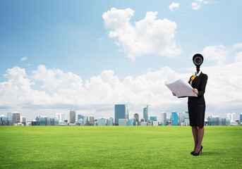 Camera headed woman standing on green grass against modern cityscape