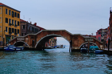 Fototapeta na wymiar Panoramic landscape view old red brick bridge over canal in Venice. Medieval colorful buildings in the background. Winter drizzle day in Venice. Famous touristic place and travel destination in Europe