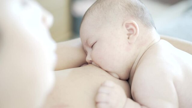 Mother breastfeeds her two-month-old newborn baby, that is almost sleeping and fixes his latching mouth position before the baby pulls away