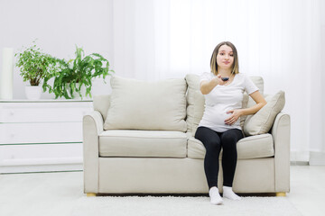 Obraz premium Pregnant woman facial expression sitting on sofa with remote control.