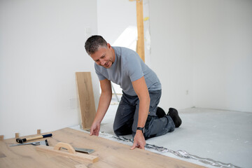Middle aged man with grey hair and grey shirt laying parquet floor in new loft, house - obrazy, fototapety, plakaty