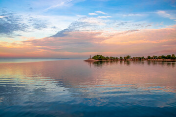 Fototapeta premium Small lighthouse on harbor quay. Dnieper river, Cherkasy, Ukraine during sunset. Picturesque colorful sky mirrored in surface water