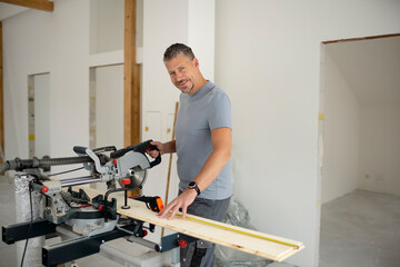 Middle aged man with grey hair and grey shirt laying parquet floor in new loft, house