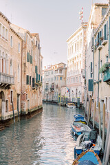 Fototapeta na wymiar The magic of Venice's city center: a canal runs through the House canyons, boats are crowded together. The water glitters turquoise and the sun reflects off the brick facades.