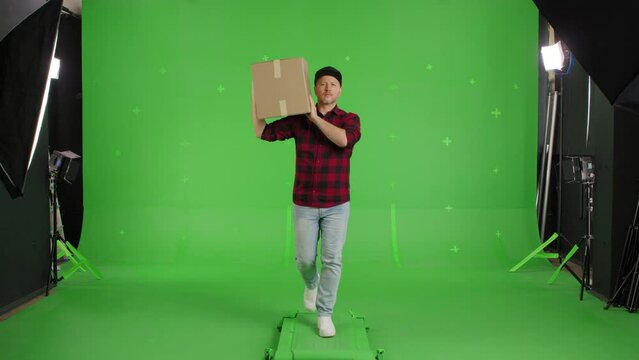 Young casual man walking on a Green Screen, Chroma Key. Man worker holding a box. Delivery concept. Forward view