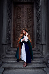 Fototapeta na wymiar Fairytale princess wearing cloak with medieval castle door on the background.