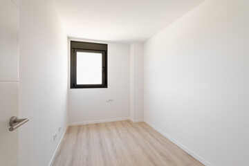 Small empty room without furniture. The floor is new light wood laminate. A window made of black plastic for airing the room. Daylight enters through the frosted glass in the window.