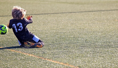 A soccer goalkeeper throwing himself to the ground to stop a ball on the pitch.