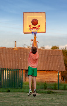 Kid boy playing basketball n sunset summer day in backyard.