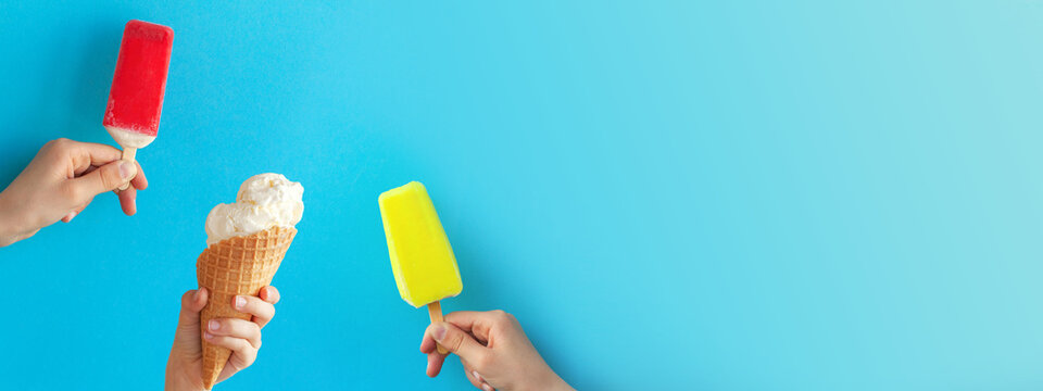 Kids hands holding cups with different ice cream and red-yellow popsicle on bright blue background.