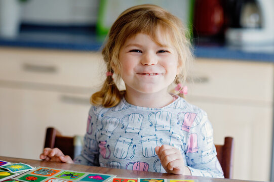 Excited smiling cute toddler girl playing picture card game. Happy healthy child training memory, thinking. Creative indoors leisure and education of kid. Family activity at home.