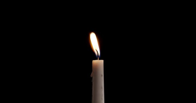 A single white candle burning.Isolated candle burning with dark background.White paraffin candle with yellow shades burns on a black background. Slow motion