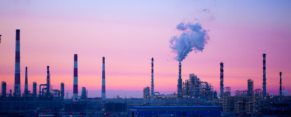 Obraz na płótnie Canvas Working oil refinery. Smoke from the factory chimney. Ecological pollution. Air emissions polluting the city. Industrial waste is hazardous to health. A large working factory in the smog at sunset.