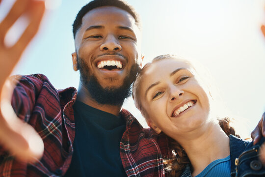 Interracial love, couple selfie and laughing at funny joke outdoors, having fun or bonding in low angle. Comic smile, romance portrait and black man and woman take pictures for happy memory together