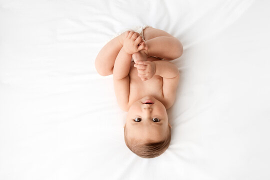 Young baby lying on white bed holding feet