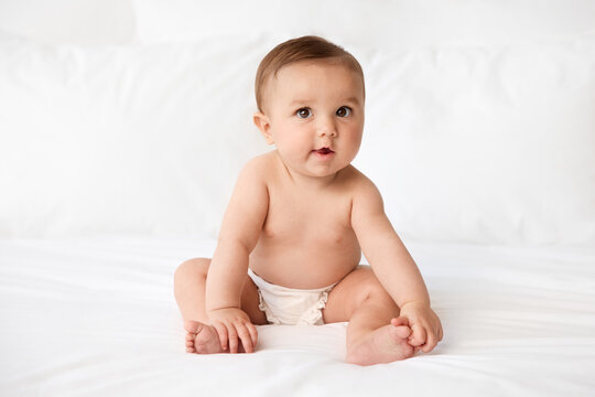 Young baby sitting on white bed holding foot