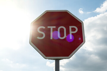 Red stop sign on metal pole on street. Road attention sign on cloudy background