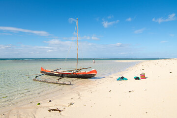 Pirogue boat trip to the Nosy Ve island, Anakao, Madagascar. View of a pirogue boat on a white sand beach with blue sky in the background. 