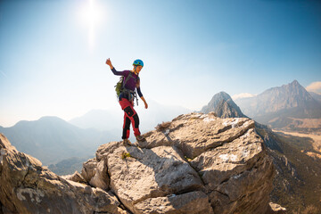 young girl climber in a helmet and with a backpack walks along a mountain range against the backdrop of mountains and climbing and hiking.