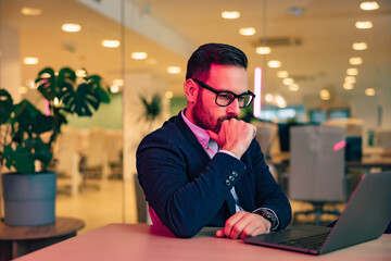 Busy male employee reading something on his laptop, sitting at the office, with glasses on.