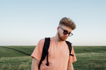 Naklejka na ściany i meble Blurred abstract photo. A stylish young man in casual clothes against the background of an endless field and a clear sky.