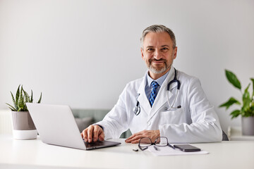 Portrait of a professional male doctor filling documents using a laptop.