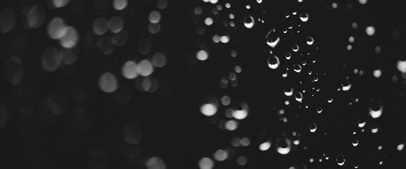 Atmospheric minimal grayscale backdrop with rain droplets on glass. Wet window with rainy drops and dirt spots closeup. Blurry minimalist monochrome background of dirty window glass with raindrops.