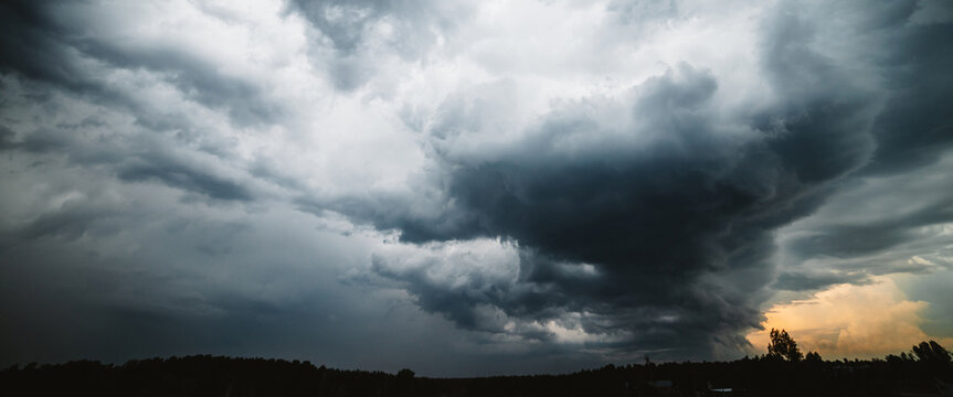 Dramatic cloudscape. Sunny light through dark heavy thunderstorm clouds before rain. Overcast rainy bad weather. Storm warning. Natural gray background of cumulonimbus. Sunlight in stormy cloudy sky. © Daniil