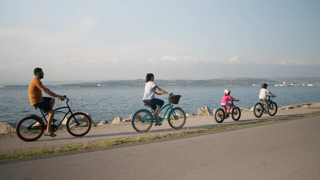 Caucasian boy and a little girl with a mother and father cycling one after another on a beautiful route along the sea coast, handheld shot. Family time concept.