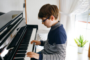 School boy with glasses playing piano in living room. Child having fun with learning to play music...