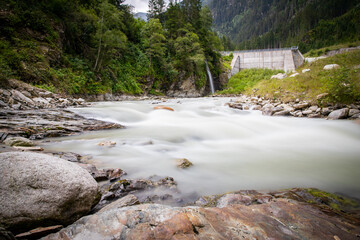 river curve with rocks in the foreground hydroelectric power station in the background small dam with trees