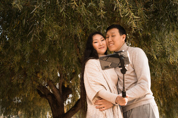 Happy smiling couple in love taking selfie photo under big green tree