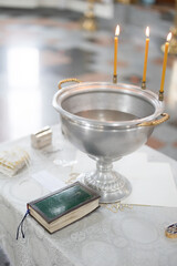 Baptismal font with wax candles is on the table near Holy Bible.